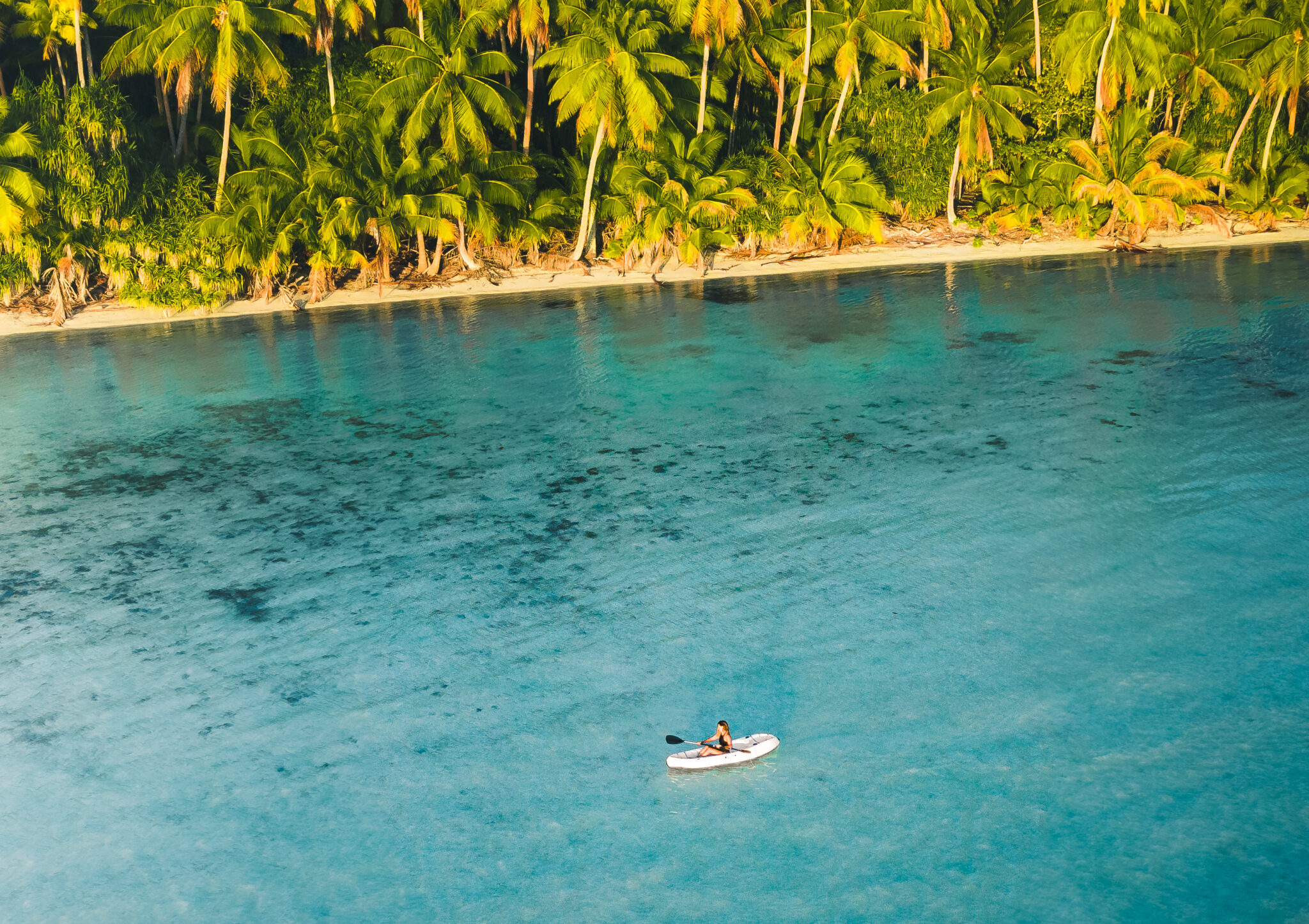 Drone shot of a woman kayaking next to an island with palm trees at our private island resort