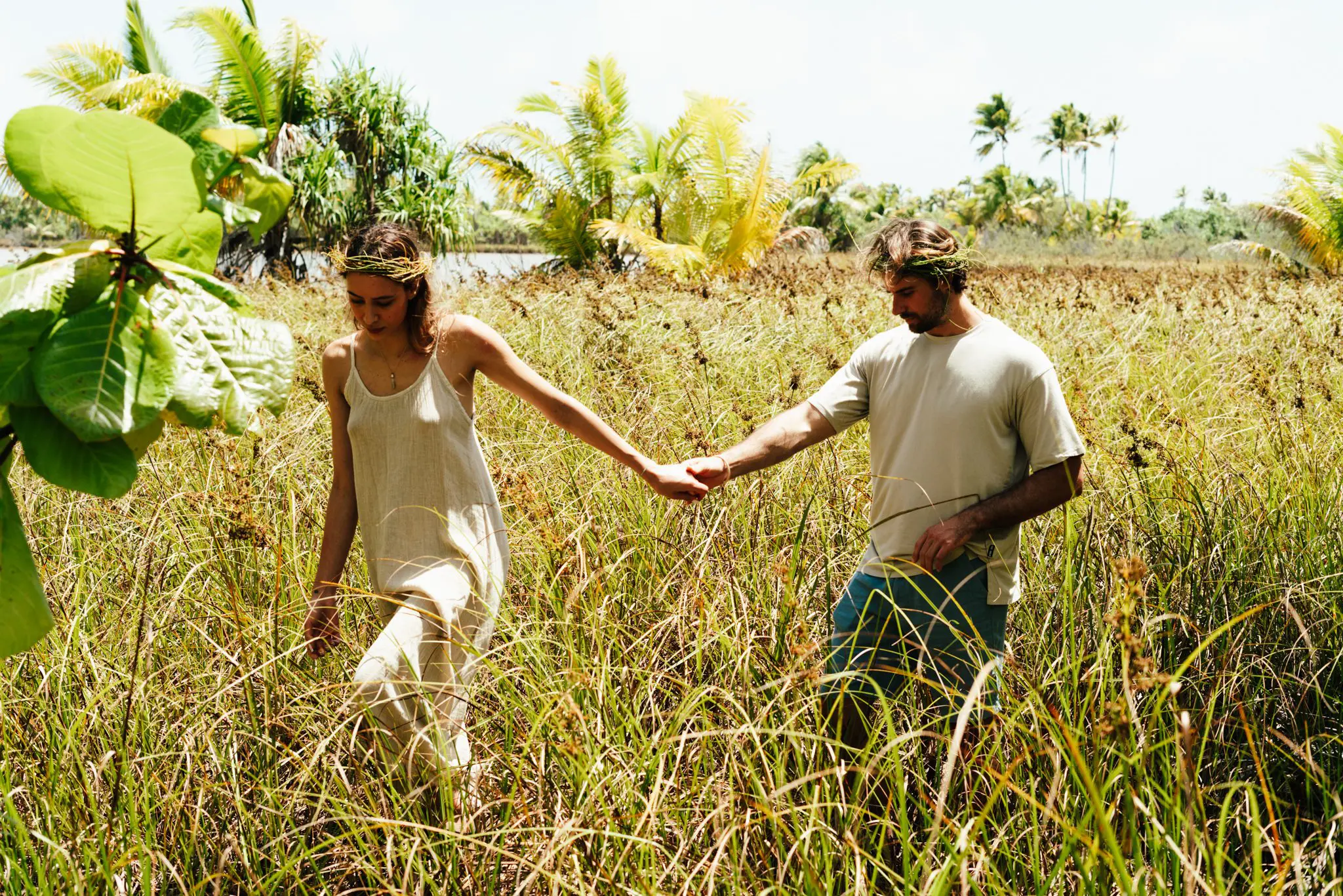 Couple holding hands and walking through tall grass wearing grass crowns at our French Polynesia resort