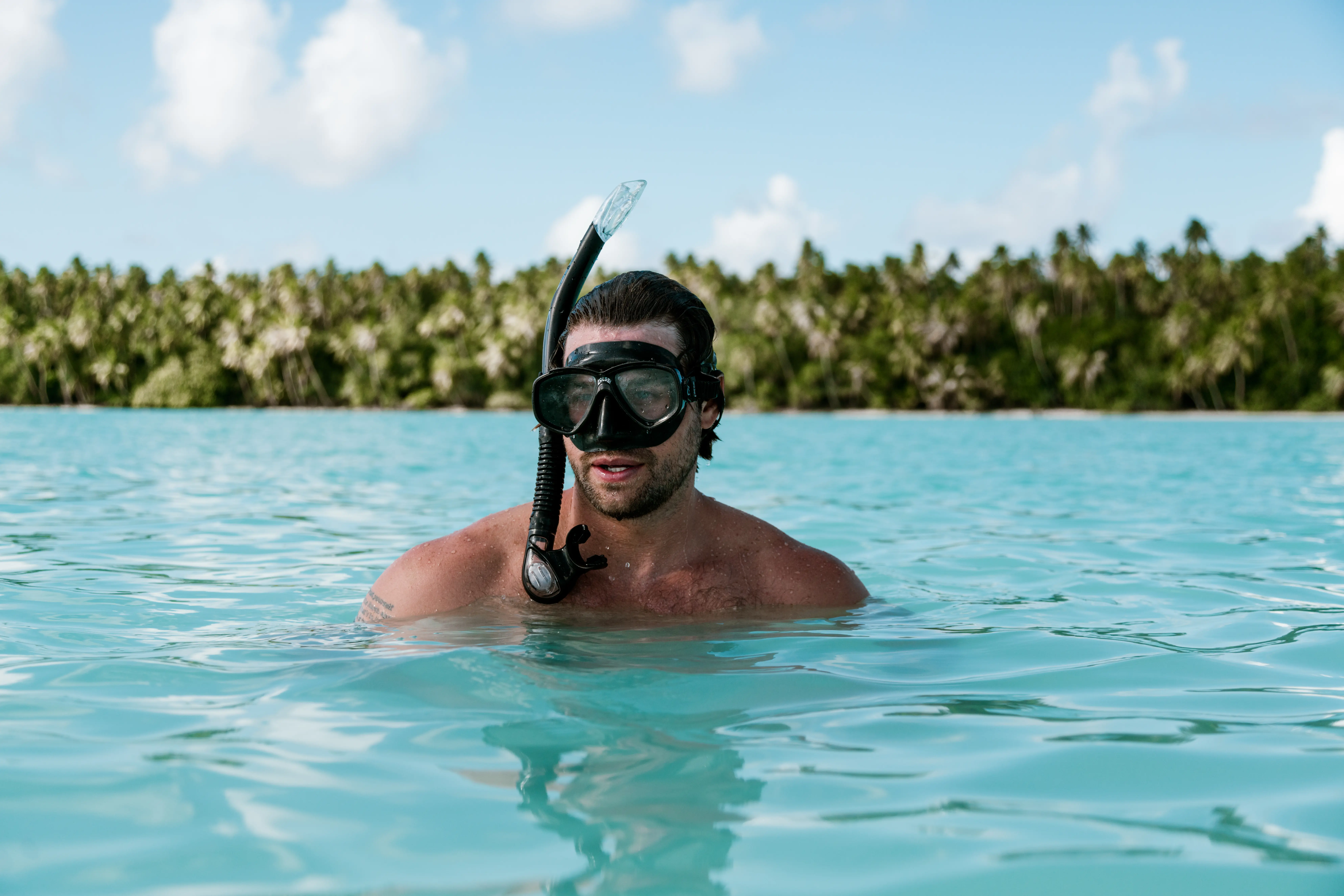 Man up to his shoulders in bright blue water with swim goggles and a snorkel at our all inclusive Tahiti resort