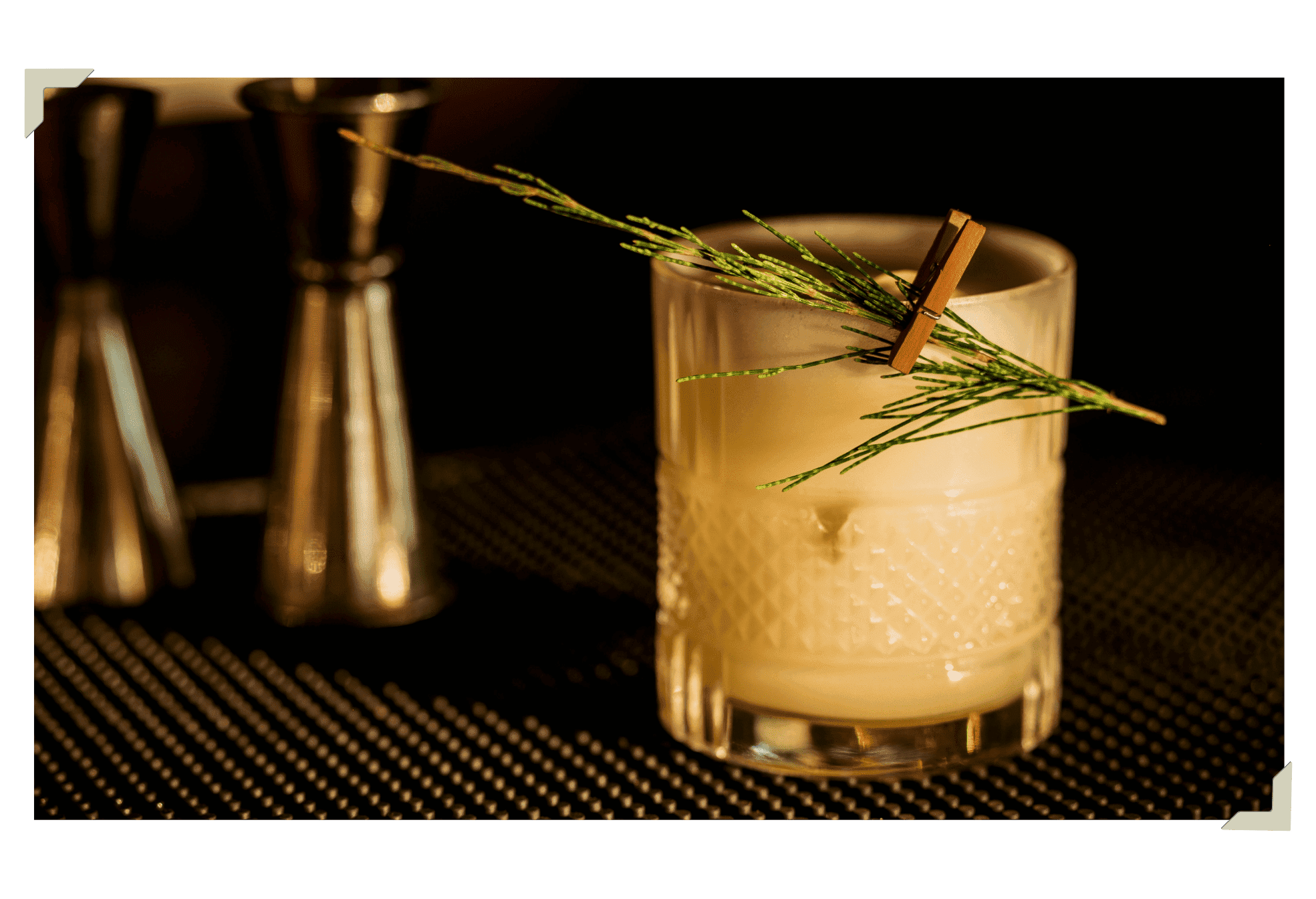 A cocktail garnished with aaito branch floating on serene water and resting on a wooden surface in soft, golden light.